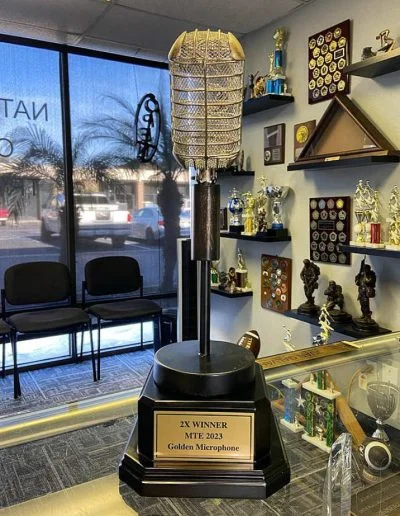 Trophy room with a large microphone trophy labeled "2x Winner MTE 2023 Golden Microphone" and various other awards.