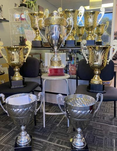 A collection of large gold and silver trophies displayed on chairs in an office setting.