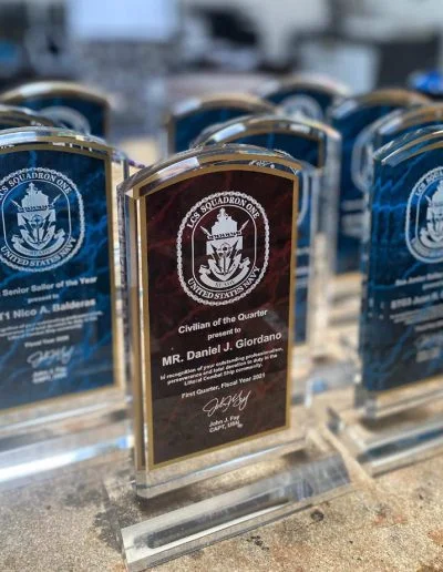 Glass awards displayed on a table, each engraved with names and achievements, featuring a nautical design.