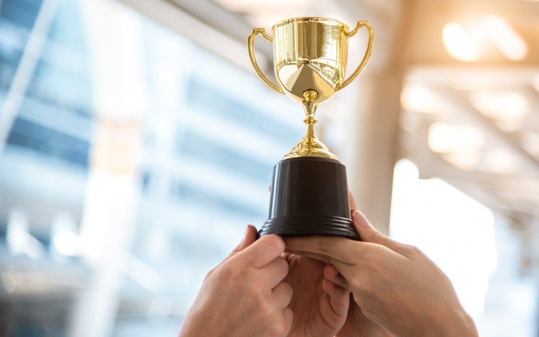 Three hands holding up a gold trophy together, symbolizing teamwork and achievement.