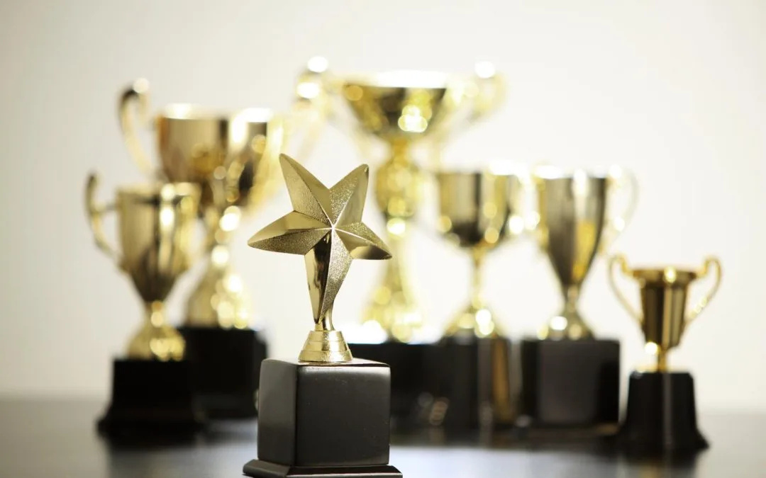 Several gold trophies, including a star-shaped one, are displayed on a black surface against a light background.